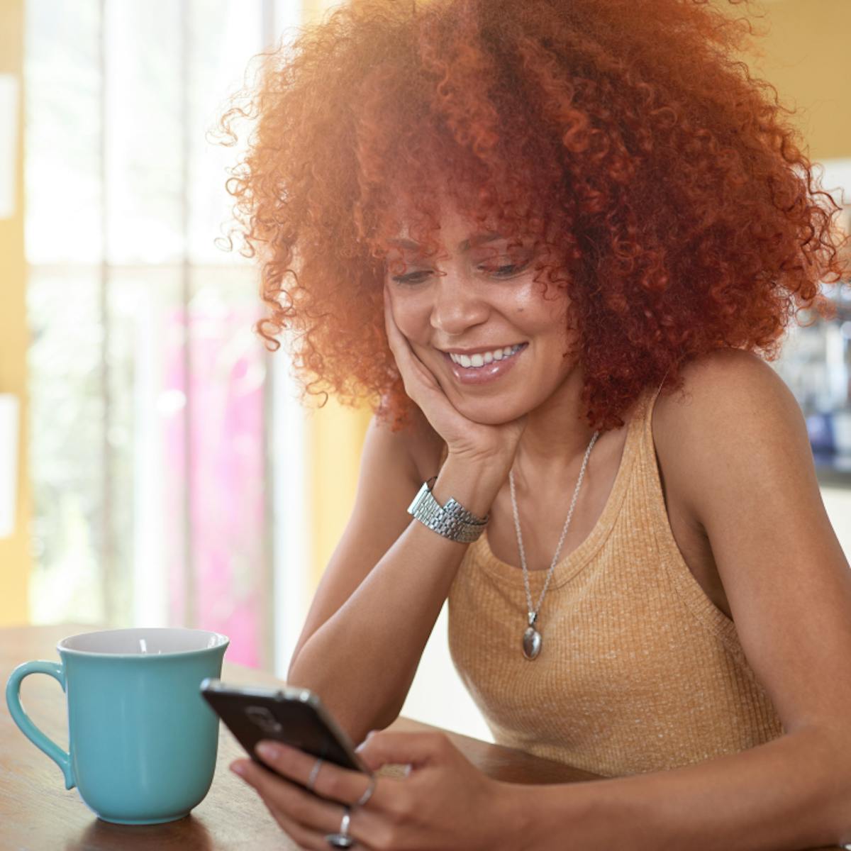 A woman sitting down looking at her phone and enjoying a cup of coffee